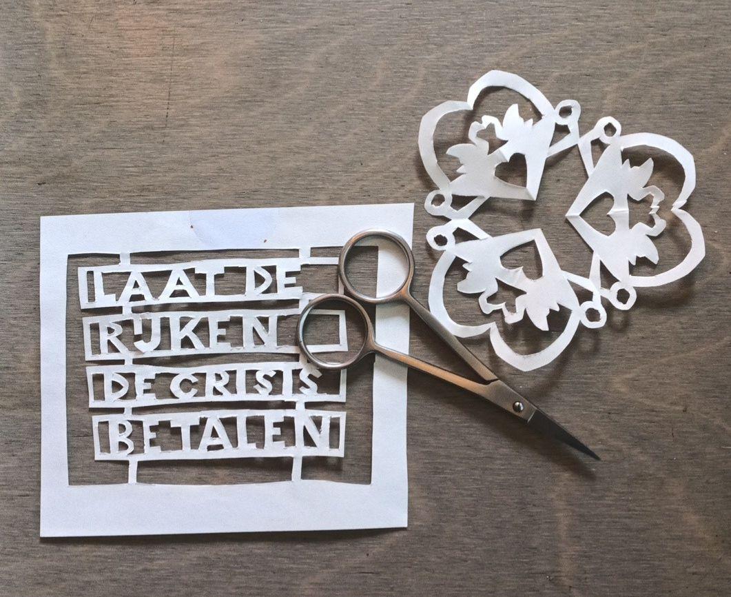 een schaartje ligt op twee knipsels. een met drie harten, met zwanen erin. de andere zegt 'laat de rijken de crisis betalen'. 